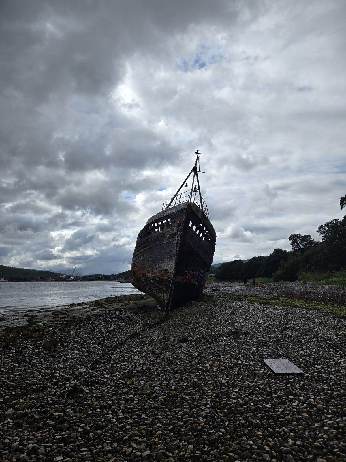 Old fishing boat wreck on the pebble shore at Corpach under a cloudy sky